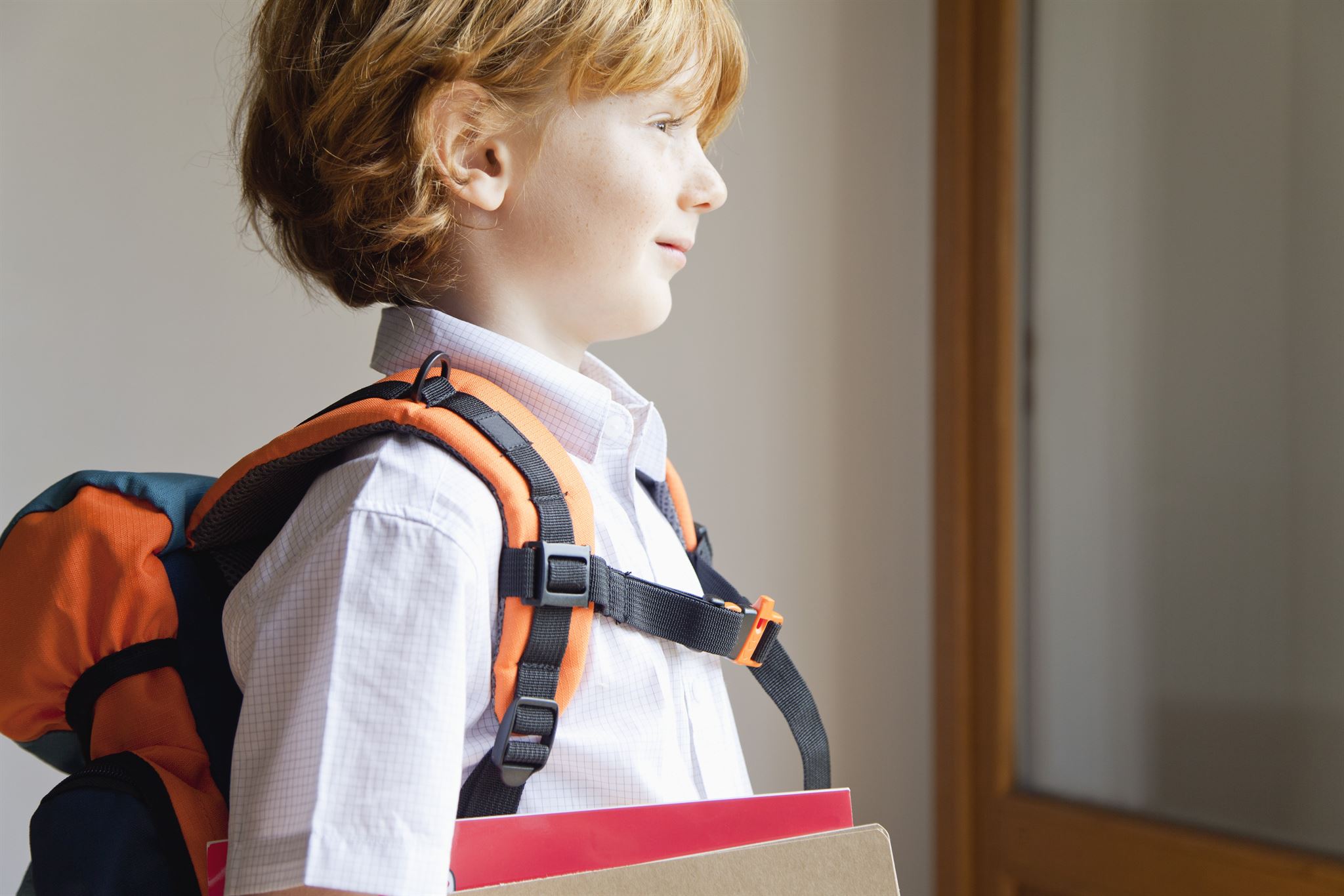 Side-view-of-young-child-wearing-backpack-holding-notebooks